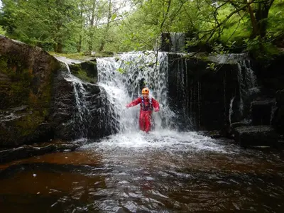 a person standing in the water in front of a waterfall at Traditional Welsh Longbarn in Aber-Brân