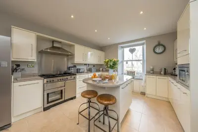 a kitchen with white cabinets and a island with bar stools at Cefn-Y-Maes in Dolgellau