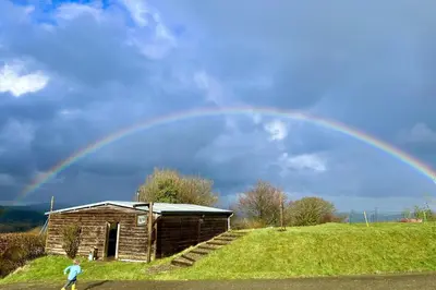 a rainbow in the sky over a wooden building at Saffir Luxury Eco Lodge, log-fired bath & views in Dihewid