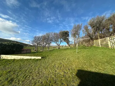 a grassy field with a fence and trees in the background at Terrace by the Tide in Aberdyfi