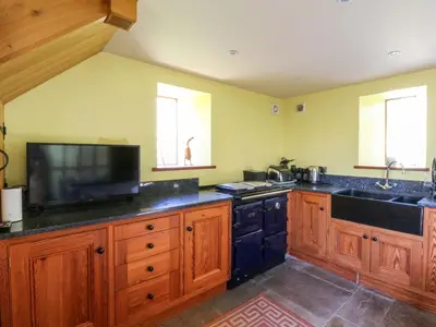 a kitchen with wooden cabinets and a sink and a tv at Maggie's Barn in Brecon