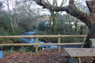 a wooden fence next to a river with a picnic table at Luxurious lodge near Barmouth in Dyffryn