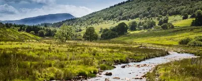 a river in a field with mountains in the background at Wunder Lodge - Snowdonia Log Cabin in Trawsfynydd