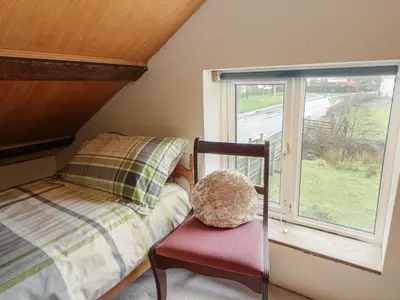 a bedroom with a bed and a chair and a window at Glanyrafon Smithy in Llandysul