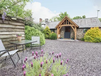 a patio with a table and flowers in front of a house at The Talkhouse Cottage in Caersws
