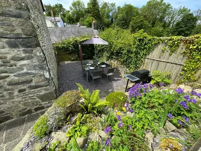 a garden with a table and an umbrella and flowers at Old Farmhouse Cottage in New Quay