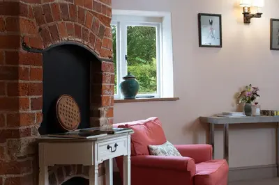a living room with a red chair and a brick fireplace at Wyvern House in Alberbury