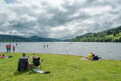 a group of people sitting on the grass near a lake at Hendre-Llangwm in Llangwm