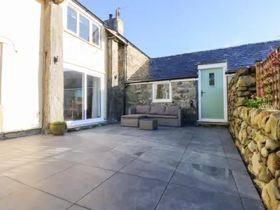 a patio with a stone wall and a couch at Yr Hen Felin in Dyffryn