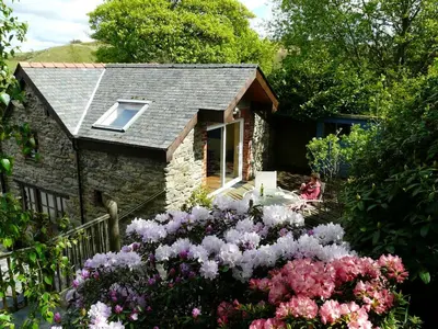 a woman sitting outside of a stone house with flowers at The Granary - Wild Swimming, Sauna, Peace & Quiet, Nr Bala in Corwen