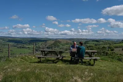 two people sitting at a picnic table on a hill at The Granary - Wild Swimming, Sauna, Peace & Quiet, Nr Bala in Corwen