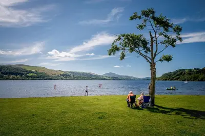 a group of people sitting under a tree near a lake at Pengwern in Cerrigydrudion