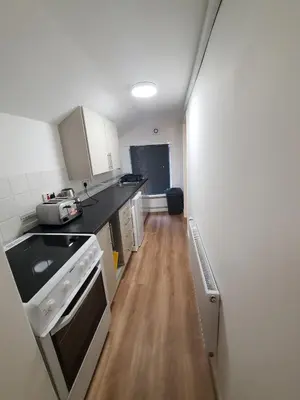 a small kitchen with white cabinets and a wooden floor at FLAT 2 Seven Cambrian Square First Floor Flat in Newtown
