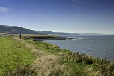 a person standing on a hill next to a body of water at Sgubor Delyn Aberystwyth in Llanrhystyd