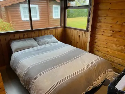 a bed in a log cabin with two windows at Log Cabin in Beautiful Snowdonia in Trawsfynydd