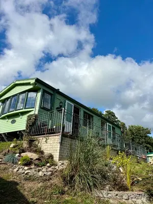 a green house sitting on top of a hill at The Woodlands Caravan in Bryn-glâs Station