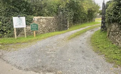 a dirt road with a sign next to a stone wall at Abbey Cottages- Red Kite Lodge in Talley