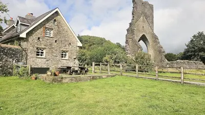 an old stone house in a field with a fence at Abbey Cottages- Red Kite Lodge in Talley