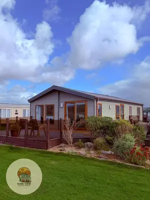 a manufactured home with a deck and lawn at Dune View Chalet in Ynys-lâs Station