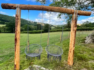 two chairs sitting on a swing in a field at Oakies Farm Stays XL in Llandovery
