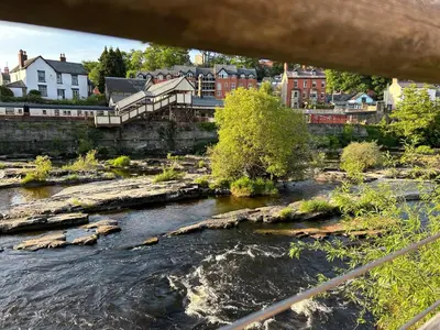 a river with rocks and a town in the background at Henllys Cottage in Corwen