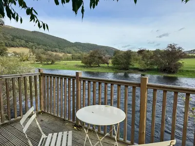 a table and chairs sitting on a deck next to a river at Henllys Cottage in Corwen