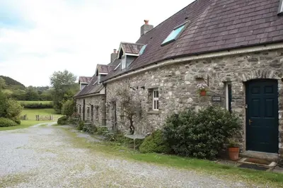 a stone house with a blue door and a gravel driveway at Abbey Cottages - Buzzards Watch in Talley