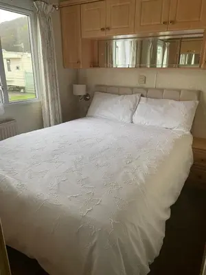 a white bed in a bedroom with a window at Family 3 Bedroom Caravan at Clarach Bay in Aberystwyth