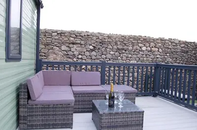 a patio with a couch and a table with a bottle of wine at Seaview Caravan f17 at Neptune Park, Tywyn in Tywyn