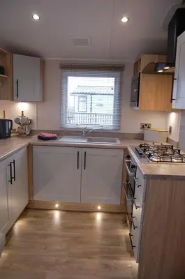 a kitchen with white cabinets and a sink and a stove at Seaview Caravan f17 at Neptune Park, Tywyn in Tywyn
