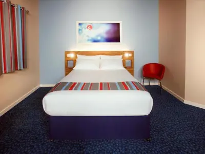 a bedroom with a large bed and a red chair at Travelodge Oswestry in Oswestry