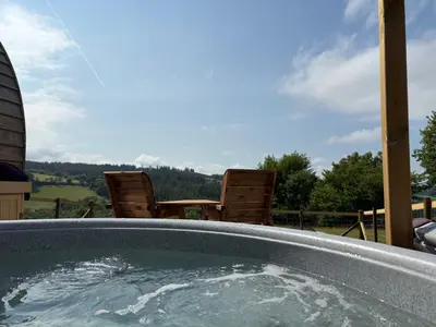 a hot tub on a patio with chairs and trees at Four Paws Glamping in Aberystwyth