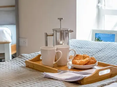 a tray with two cups and a plate of pastries on a bed at Seagrass Cottage in Aberdyfi