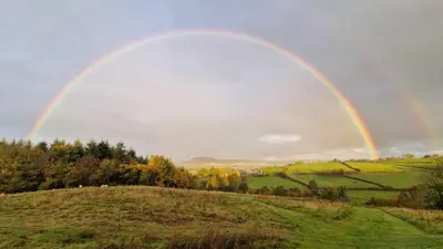 a rainbow over a green field with a hill at Oak Hill Escape in Welshpool