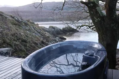 a bath tub next to a tree next to a body of water at Salt Marsh Cabin - Hot tub-Sauna in Barmouth