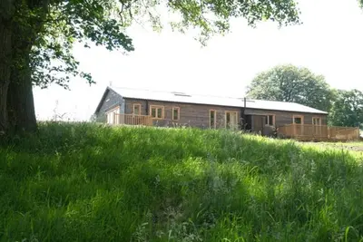 a house on top of a grassy hill with a tree at Alder Barn in Clun