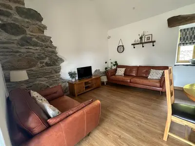 a living room with leather couches and a stone wall at Y Sgubor Bryn Banon in Bala