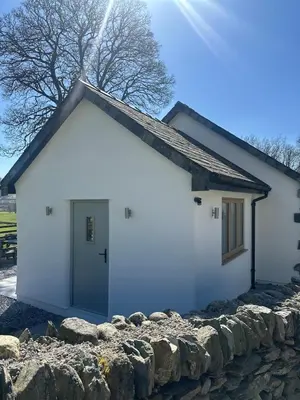 a white house with a stone wall at Y Beudy Bach in Llanfor
