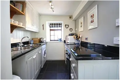 a kitchen with white cabinets and black counter tops at Cosy River Cottage in Brecon with a Fireplace in Merthyr Cynog