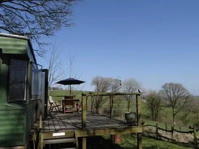 a wooden deck with a table and an umbrella at Canad Adar - Song of the Birds - Teifi Valley in Llanwenog