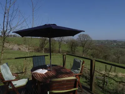 a table and chairs with an umbrella on a deck at Canad Adar - Song of the Birds - Teifi Valley in Llanwenog