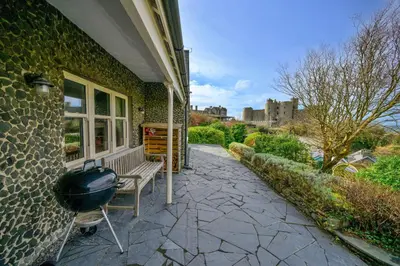 a house with a grill and a bench with a castle in the background at Finest Retreats - Bryn Awelon in Harlech