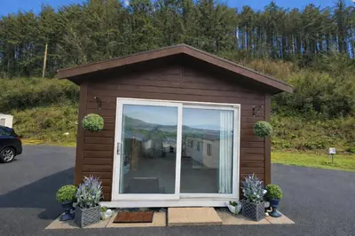 a small shed with a window and potted plants at Welsh Coast Seaview 2 Bedroom Wooden Lodge at Clarach Bay in Aberystwyth