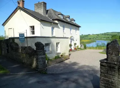a large white house with a river behind it at Aberllynfi Riverside Guest House in Glasbury