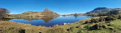 a lake in the middle of a field with mountains at Dinas in Llanbedr