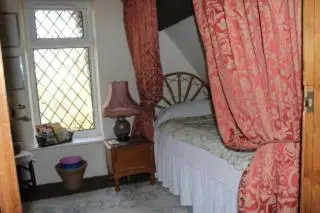 a bedroom with a bed with red curtains and a window at Parrs cottage in Wollaston