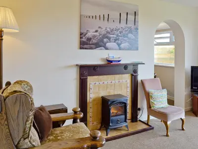a living room with a fireplace and a chair at Fairlawns in Fairbourne