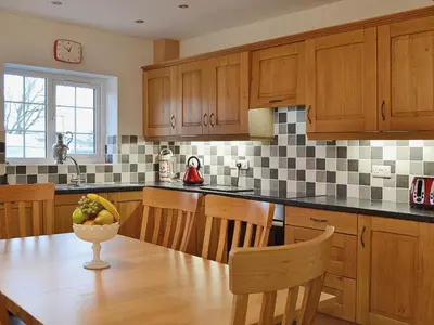 a kitchen with wooden cabinets and a table with a bowl of fruit at Maes Rheidol in Capel Bangor