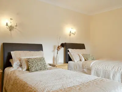 a bedroom with two beds and a vase with flowers at 4 Pengraig Draw in Llanychaiarn
