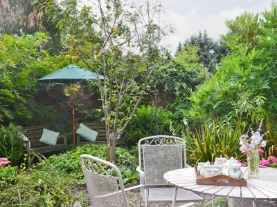 a table with chairs and an umbrella in a garden at Friary Cottage in Ludlow